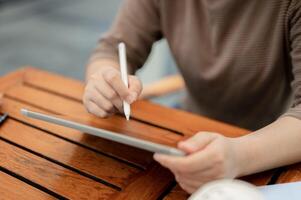 A woman holding a tablet pen and writing on her digital tablet, working remotely at a cafe. photo