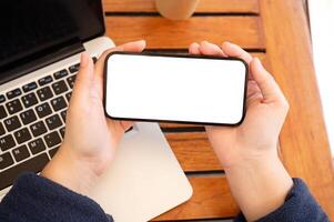 A top view image of a woman holding a white-screen smartphone mockup in a horizontal position. photo