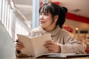 A woman is looking out the window and daydreaming while reading a book in a coffee shop. photo