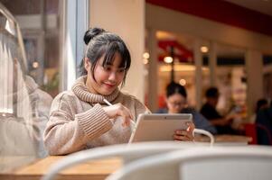An attractive, happy Asian female is working remotely at a cafe co-working space, using her tablet. photo