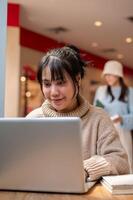 An attractive Asian woman in a comfy sweater is working remote at a cafe, working on her laptop. photo