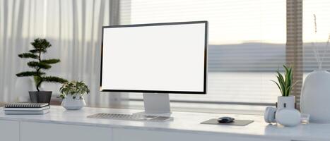 A computer desk featuring a computer with a white-screen mockup on a table in a modern white room. photo