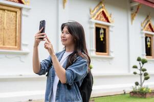 A happy Asian female traveler is taking a picture of a Thai temple with her smartphone. photo