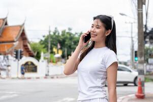 A beautiful Asian woman is talking on the phone while standing by the street in the city. photo