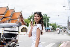 A positive Asian woman is talking on the phone while standing by the street, smiling at the camera. photo