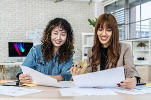 Two business young asian woman working together in office with reports and tablet, colleagues discuss financial data analyzing documents marketing project result talk business conversation photo