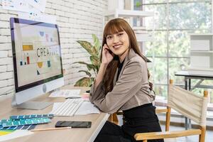 Asian young woman graphic designer smiling and looking at camera sitting at the desk with pc and tablet computer while working in office, Artist Creative Designer Illustrator Graphic Skill Concept photo