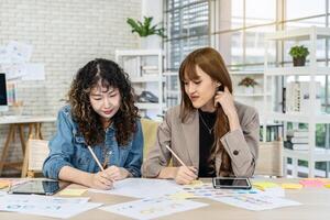 Two business young asian woman working together in office with reports and tablet, colleagues discuss financial data analyzing documents marketing project result talk business conversation photo