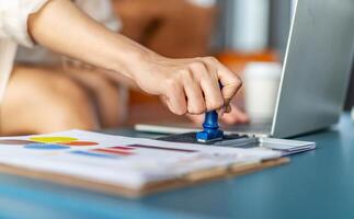 Close-up Of Business woman is hand stamping with approved stamp on document on the table and laptop and a cup with a drink, Concept of paperwork and business, agreement, seal on document photo