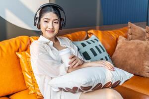 Weekend relax,Young asian Woman In Headphones Sitting In Couch At Home Listening Favorite Music and enjoying cup of coffee on sofa, Concept Of Relax And Meditation photo