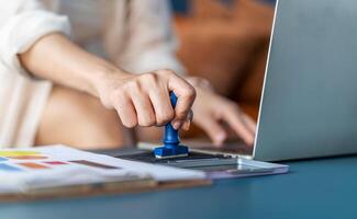 Close-up Of Business woman is hand stamping with approved stamp on document on the table and laptop and a cup with a drink, Concept of paperwork and business, agreement, seal on document photo