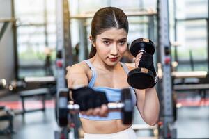 Confident young asian fitness woman doing exercises with dumbbells, Smiling girl doing sports indoors with dumbbells lifting weights. Fit fitness girl in sportswear exercising inside to slim down. photo