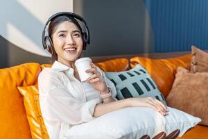 Weekend relax,Young asian Woman In Headphones Sitting In Couch At Home Listening Favorite Music and enjoying cup of coffee on sofa, Concept Of Relax And Meditation photo