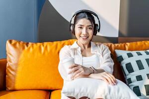 Weekend relax,Young asian Woman In Headphones Sitting In Couch At Home Listening Favorite Music and enjoying cup of coffee on sofa, Concept Of Relax And Meditation photo