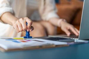 Close-up Of Business woman is hand stamping with approved stamp on document on the table and laptop and a cup with a drink, Concept of paperwork and business, agreement, seal on document photo
