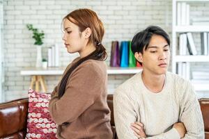 Photo of resentful asian guy and girl acting like arguing couple and not speaking to each other, while sitting together on couch at home
