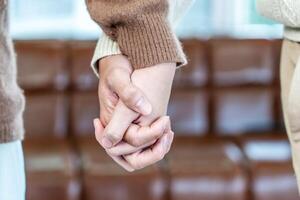 Close up of hand young happy loving couple guy and girl standing in front of big window, back to camera front view of an affectionate couple looking out of window while holding hand photo