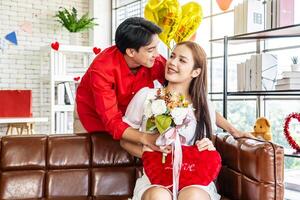 Young asian man or boyfriend surprise and giving flowers at his girlfriend sitting on the sofa at home for the Valentine's day, happy couple with bunch of flowers in house, holidays and people photo