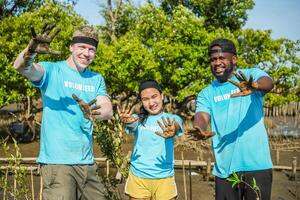 Group of volunteer showing hands soiled in mud sign smiling look at camera helpers planting trees in mangrove forest for environmental protection and ecology, reduce global warming, Charity work photo