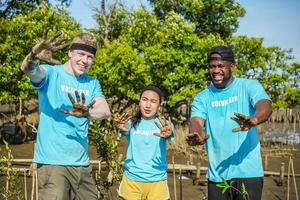 Group of volunteer showing hands soiled in mud sign smiling look at camera helpers planting trees in mangrove forest for environmental protection and ecology, reduce global warming, Charity work photo