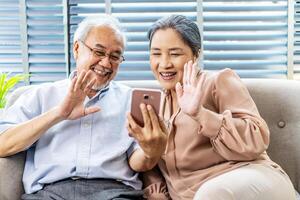 Happy elderly retired couple making call with mobile phone, gesturing hi, having pleasant conversation,chatting with grown up children grandchildren using wireless internet connection at home photo