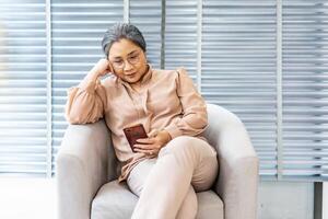Pleasant senior older lady resting on couch at home, older middle aged female customer holding smartphone using mobile app, texting message, search ecommerce offers on cell phone technology device photo