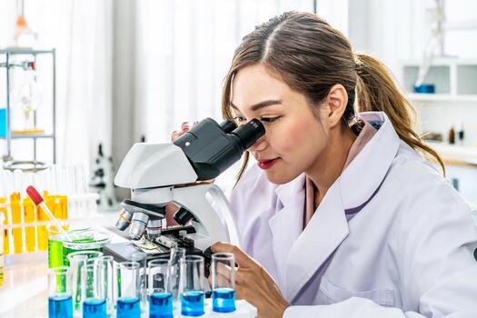 Smiling young asian woman wearing scientist uniform working at scientist laboratory with looking through a microscope in a laboratory. Young scientist doing some research. photo