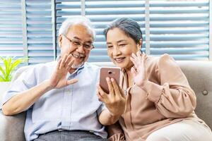 Happy elderly retired couple making call with mobile phone, gesturing hi, having pleasant conversation, chatting with grown up children grandchildren using wireless internet connection at home photo