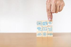 Businessman hand with wood cube block and icon symbol to 5G network high speed mobile internet new age network, mixed media, World wide business photo