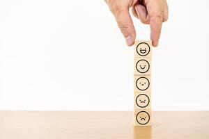 Hand of a businessman chooses a smiley face icon on wood block cube, The best excellent business services rating customer experience, Satisfaction survey concept, Service rating photo