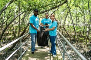 Tres voluntarios en trabajo mono recoger basura en bosque en el plastico bolsa. de cerca durante acción. limpieza de naturaleza desde desperdiciar. ambiental asistencia. basura colección en bosque foto