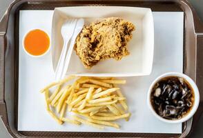Top view of crispy fried chicken, french fries, chili sauce and soft drink on the side, in the tray, photographed overhead with natural light photo