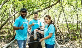 Three volunteers in work overalls collect garbage in forest in plastic bag. Close-up during action. Cleaning of nature from waste. Environmental assistance. Garbage collection in forest photo
