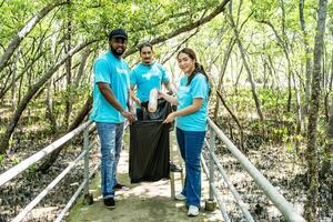 Tres voluntarios en trabajo mono recoger basura en bosque en el plastico bolsa. de cerca durante acción. limpieza de naturaleza desde desperdiciar. ambiental asistencia. basura colección en bosque foto