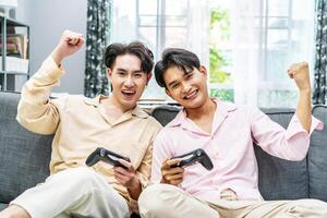 Two young males relax on weekend sit on couch enjoy console game push buttons on controllers. Two Male Players spend free time together play online game having fun photo