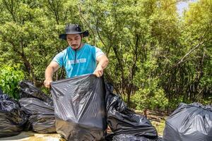 One volunteers in work overalls collect garbage in forest in plastic bag. Close-up during action. Cleaning of nature from waste. Environmental assistance. Garbage collection in forest photo