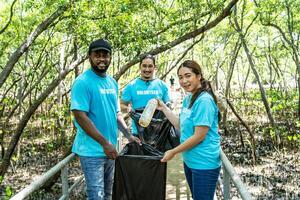 Tres voluntarios en trabajo mono recoger basura en bosque en el plastico bolsa. de cerca durante acción. limpieza de naturaleza desde desperdiciar. ambiental asistencia. basura colección en bosque foto