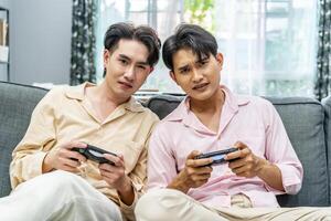 Two young males relax on weekend sit on couch enjoy console game push buttons on controllers. Two Male Players spend free time together play online game having fun photo