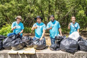 Four volunteers in work overalls collect garbage in forest in plastic bag. Close-up during action. Cleaning of nature from waste. Environmental assistance. Garbage collection in forest photo