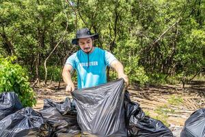 One volunteers in work overalls collect garbage in forest in plastic bag. Close-up during action. Cleaning of nature from waste. Environmental assistance. Garbage collection in forest photo