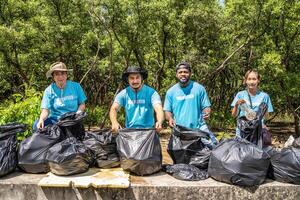 Four volunteers in work overalls collect garbage in forest in plastic bag. Close-up during action. Cleaning of nature from waste. Environmental assistance. Garbage collection in forest photo