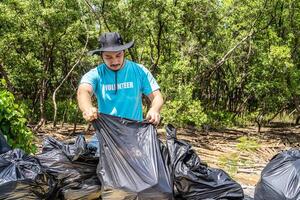 One volunteers in work overalls collect garbage in forest in plastic bag. Close-up during action. Cleaning of nature from waste. Environmental assistance. Garbage collection in forest photo
