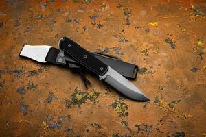A modern hunting knife with a rubberized handle and a plastic sheath on a orange back. Melee weapons for self-defense and survival. photo