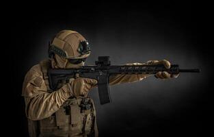 Modern soldier in full ammunition with weapons in his hands on a black background. The military aims from an automatic rifle. photo