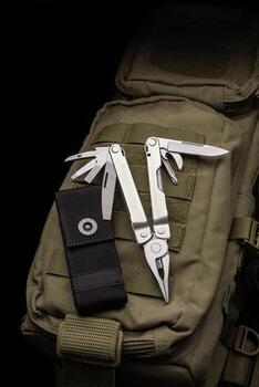 Modern multitool with many tools. A portable multitasking tool lie on a khaki-coloured military backpack. Dark back. photo