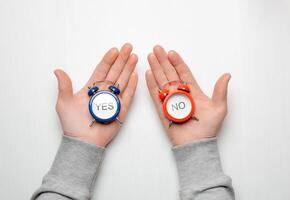 men's hands hold a red and blue alarm clock with the words yes and no. concept of choice and decision making photo