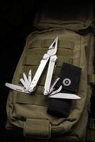 Modern multitool with many tools. A portable multitasking tool lie on a khaki-coloured military backpack. Dark back. photo