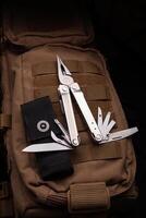 Modern multitool with many tools. A portable multitasking tool lie on a desert-colored military backpack. photo