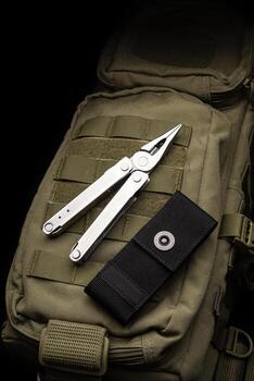 Modern multitool with many tools. A portable multitasking tool lie on a khaki-coloured military backpack. Dark back. photo