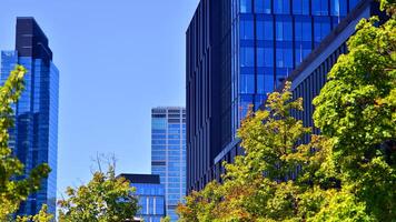 City life, urban landscape and ecology. Modern office complex with glass facades and smooth lines against backdrop of green trees, concept of modern architecture. Organically building into nature. photo